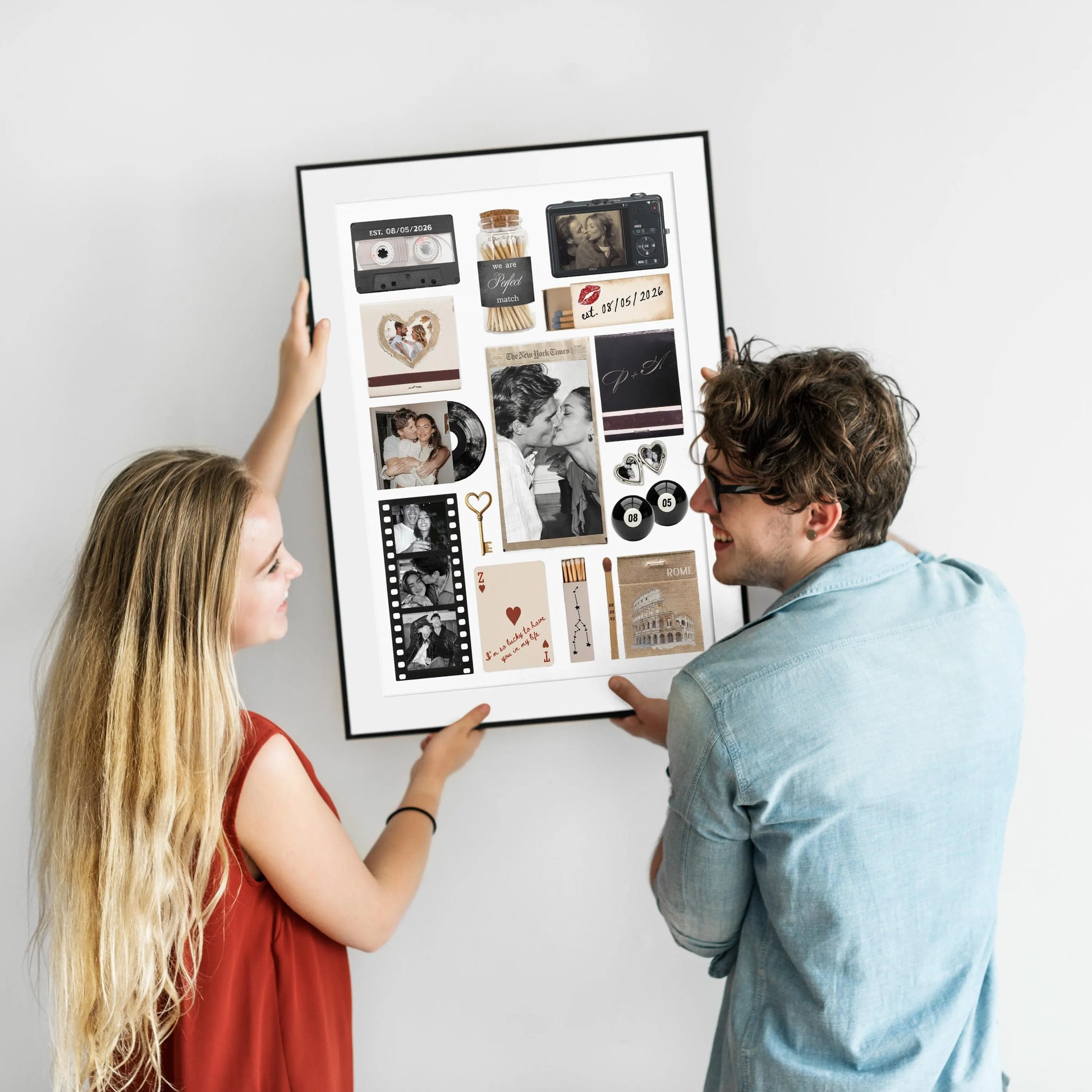 Ein lächelndes Paar hält gemeinsam ein gerahmtes, personalisiertes Matchbook Poster mit individuellen Fotos an eine weiße Wand.