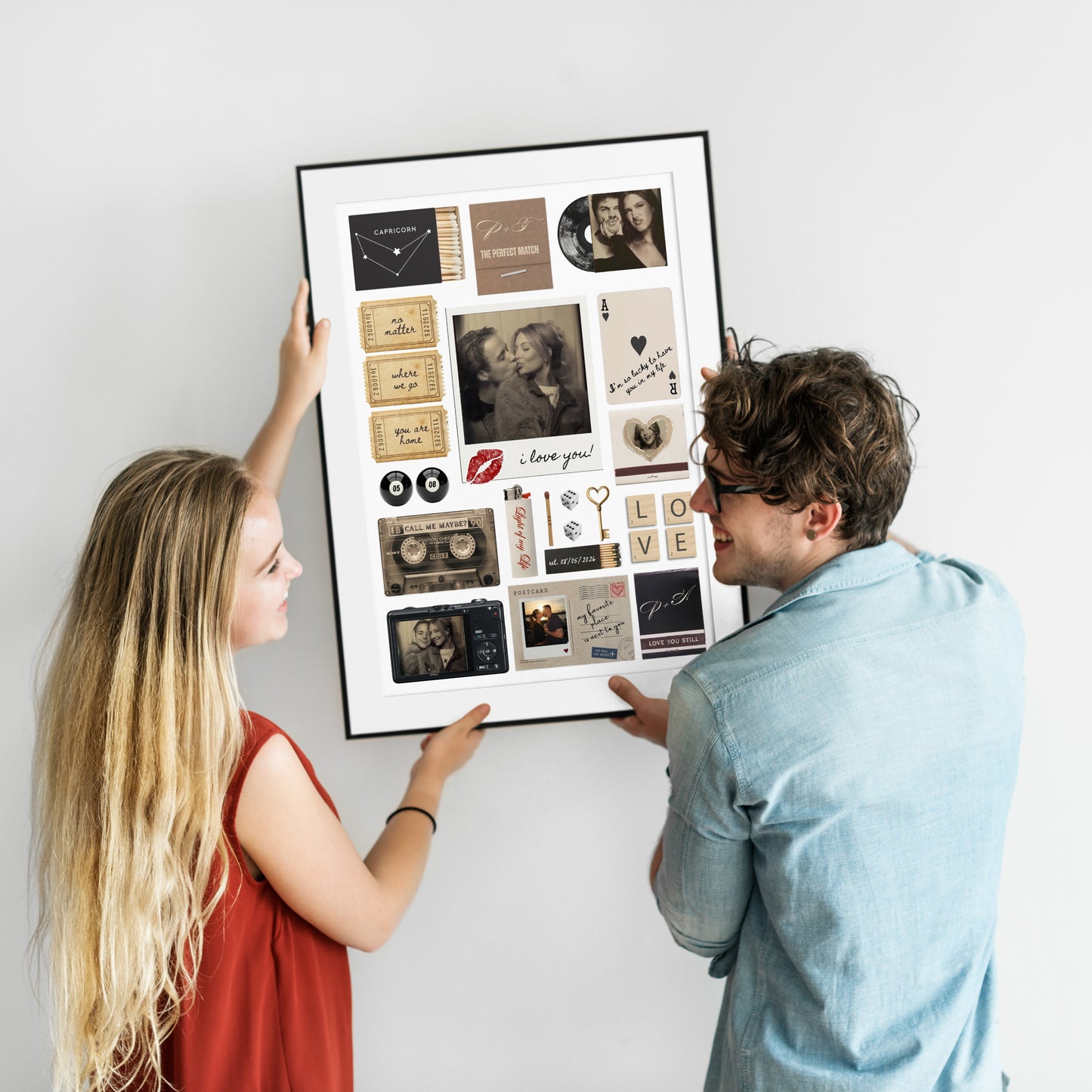 Ein Paar hängt gemeinsam ein gerahmtes, personalisiertes Matchbook-Poster mit eigenen Fotos an eine weiße Wand.