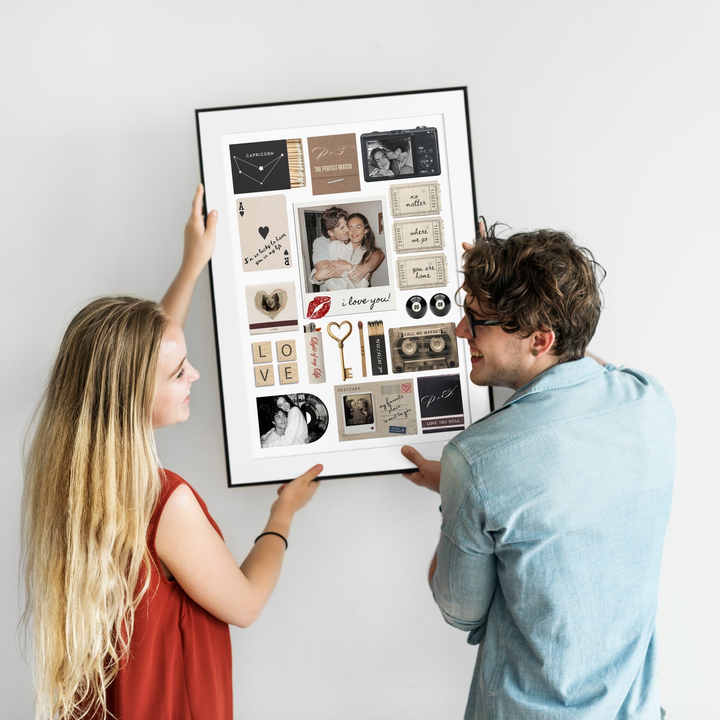 Ein lächelndes Paar hängt gemeinsam ein großes, gerahmtes Matchbook-Poster mit persönlichen Fotos an eine weiße Wand.