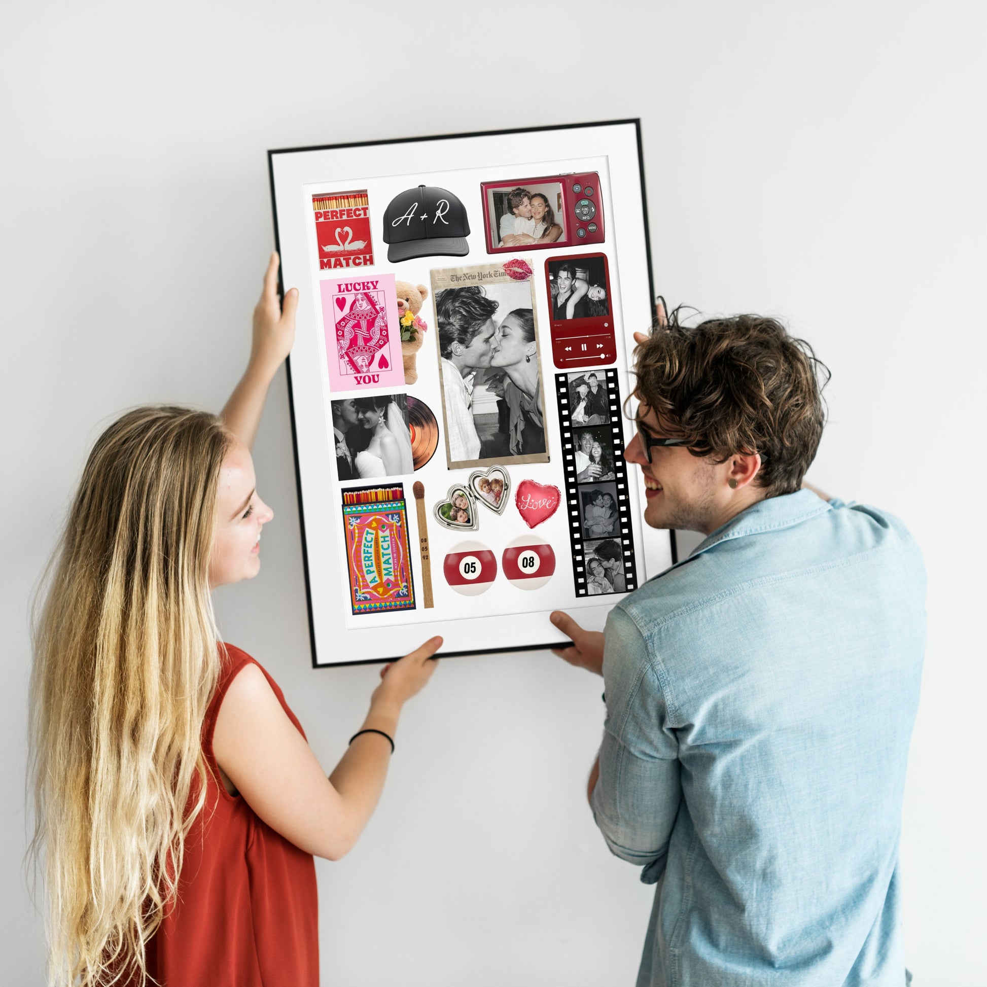 Ein lächelndes Paar hält gemeinsam ein gerahmtes, personalisiertes Matchbook-Poster mit eigenen Fotos an eine weiße Wand.