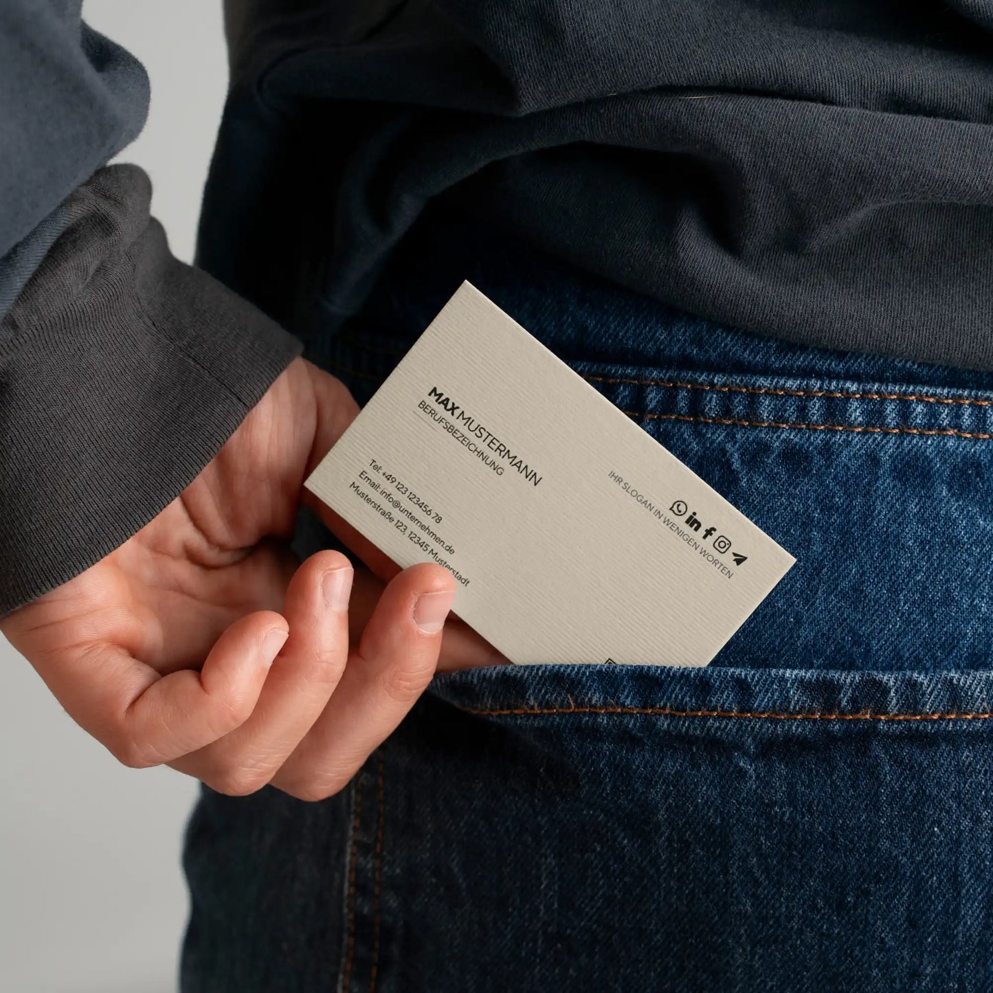 Person hält eine minimalistische Visitenkarten Vorlage in Beige in der Hosentasche mit QR-Code, Kontaktdaten und personalisierbarem Canva Design – Louvion.de